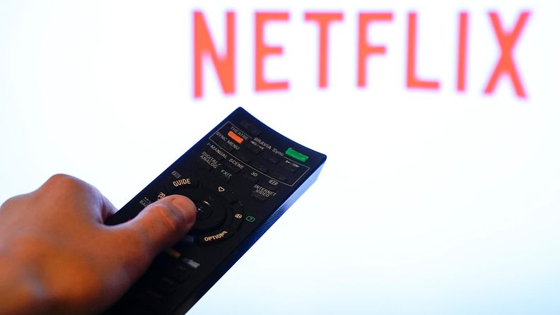 Käsi osoittaa kaukosäätimellä ruudulle, jossa loistaa Netflixin punainen logo valkoisella taustalla.