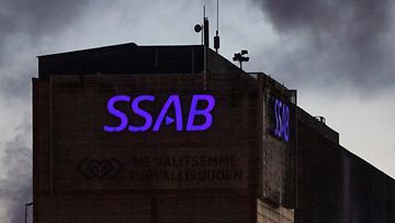 SSAB:n violetti logo hohtaa tehtaan kyljessä pimeydessä.