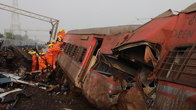 Oranssipukuiset pelastustyöntekijät tutkivat murskaantunutta junaa.