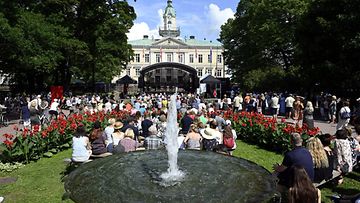 Väkijoukko istuu Porin Raatihuoneen edustalla aurinkoisena päivänä SuomiAreenan aikana.