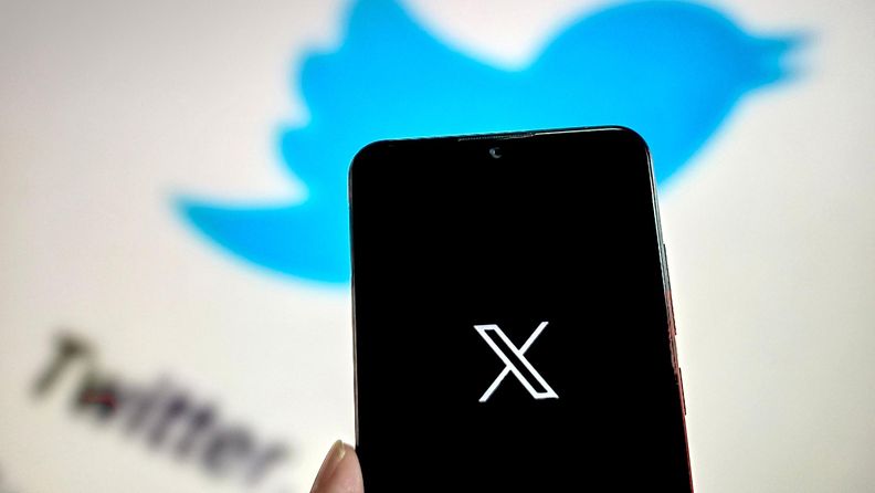 X logo mustalla puhelimen ruudulla, taustalla möllöttää Twitterin lintulogo.