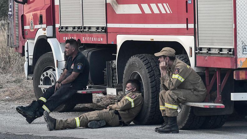 Palomiehet lepäävät paloautoa vasten nokisissa univormuissaan.