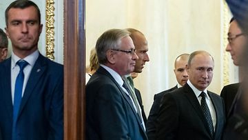 Henkivartija seisoo etualalla oven takana, kun Putin valmistautuu astumaan ovesta sisälle. 