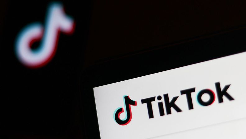 TikTokin logo puhelimen näytöllä ja TikTokin verkkosivuilla kannettavan tietokoneen näytöllä. Kuvituskuva.