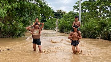 Two men carry children on their shoulders as they wade through flood waters in Pyinmana, Naypyidaw, Myanmar, 13 September 2024. 